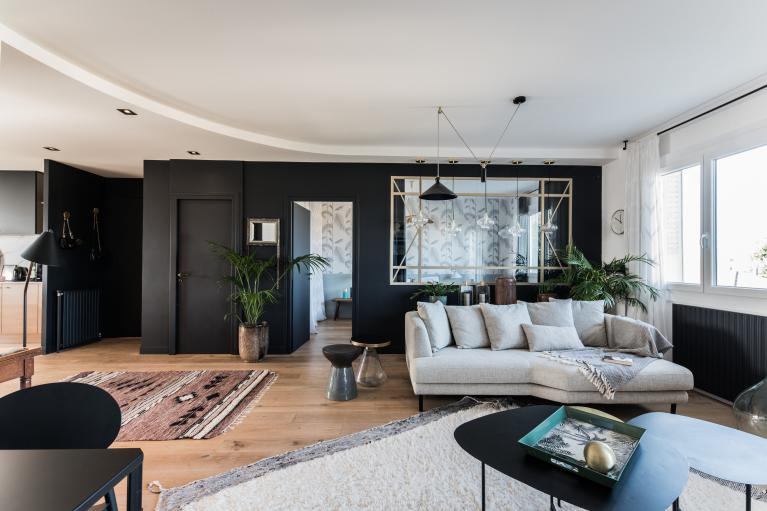 Salon avec un canapé gris. Les murs sont noirs et le sol est en parquet marron pour apporter du contraste à la pièce. Les meubles noirs apportent à la pièce un côté moderne chic.